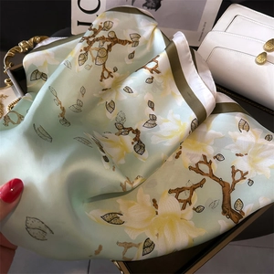 Detailed texture of light green silk scarf featuring elegant white magnolia flower prints