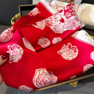 Close-up of elegant red silk scarf with white rose floral print on luxury tray