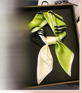 Detail of satin silk scarves in green and orange geometric patterns on a black display tray