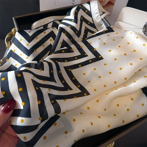 Détail d'un foulard en soie à rayures noires et pois jaunes dans un plateau de luxe