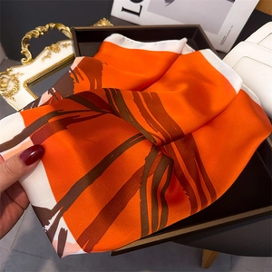 Detail of orange satin scarf with abstract print and white edges on a wooden tray