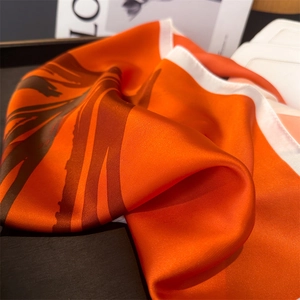 Detail of silk-like square scarf with orange and brown stripes and smooth texture