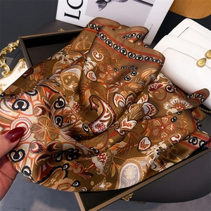 Gros plan d'un foulard carré en soie avec motifs paisley marron sur un plateau décor