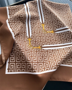 Dettaglio di un foulard in seta marrone con motivi di morsi e catene dorate