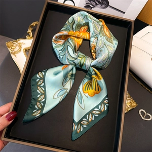 Detail view of a mint green silk floral scarf tied in a bow on a luxury tray