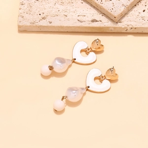 Detailed close-up of heart-shaped gold enamel earrings with baroque pearl pendants