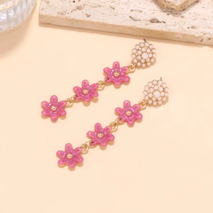 Close-up of pink enamel flower earrings with pearls on a textured beige background