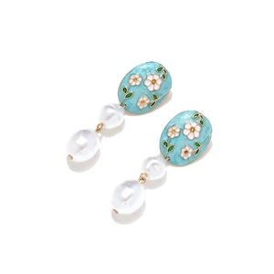 Détail de boucles d'oreilles fleur émaillée avec perles baroques et finition bleue claire