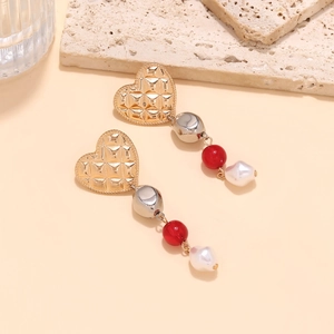 Golden heart earrings with red beads and baroque pearls on a textured beige surface