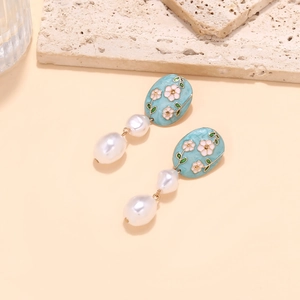 Détail macro de boucles d'oreilles perles baroques et fleurs en émail bleu sur fond beige