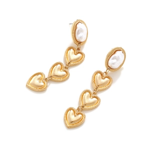 Detail of baroque pearl studs and triple tiered gold heart drop earrings on white background
