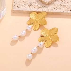 Vue détaillée de boucles d'oreilles fleur dorées avec perles baroques sur pierre
