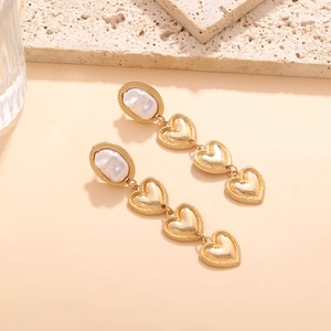 Elegant gold layered heart drop earrings with baroque pearl on warm beige stone background