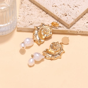 Detail of golden conch earrings with baroque pearls on a textured stone surface