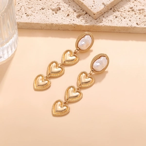 Close-up of triple layered gold hearts with a baroque pearl on a long drop earring