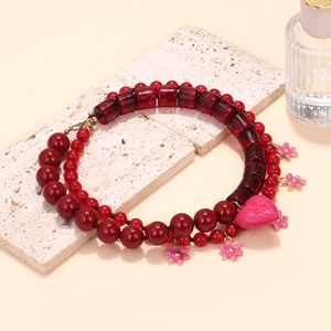 Detail of red beaded necklace with heart pendant and flower charms on stone background