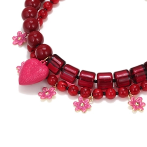 Close-up of beaded necklace with red resin beads and pink enamel floral heart charms