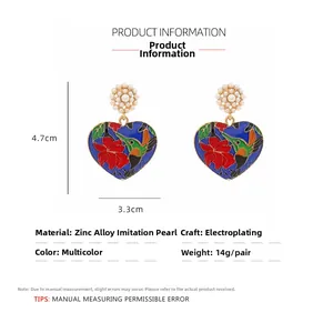 Detail view of colorful enamel hummingbird and flower pattern on heart drop earrings