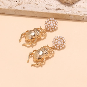 Détail macro de boucles d'oreilles scarabée dorées avec perles sur fond de pierre
