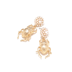Détail de boucles d'oreilles scarabée dorées vintage avec texture métal et perles nacrées