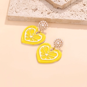 Enamel lemon heart drop earrings with pearl clusters on a beige stone display