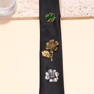 Detailed close-up of clover, daisy, and flower pins set on a black tie accessory