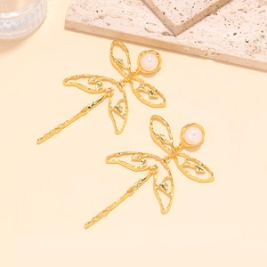 Detailed close-up of golden dragonfly earrings with pearls and hollow wings