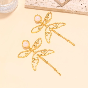 Detailed view of vintage gold dragonfly earrings with pearl accents on stone background