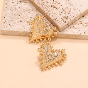 Vintage golden heart earrings with hammered texture and beaded edges on a beige stone