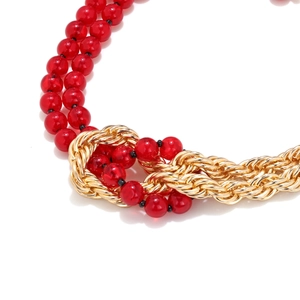 Detailed view of red resin beads intertwined with a gold braided metal chain knot