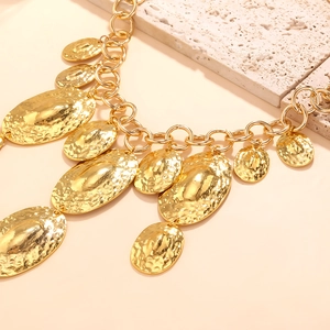 Gros plan sur un collier à grosse chaîne dorée avec pendentifs ovales à texture martelée