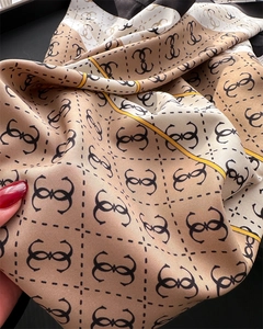 Detail of elegant beige silk scarf featuring black monogram print and striped border