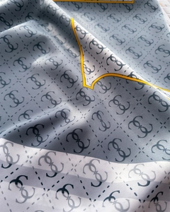 Close-up of silk-textured blue square scarf featuring luxury letter pattern and gold trim