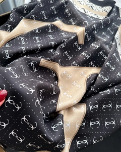 Detail of luxury silk scarf showing black and gold monogram pattern with satin luster