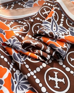 Close-up of silk scarf fabric showing orange floral prints and geometric patterns
