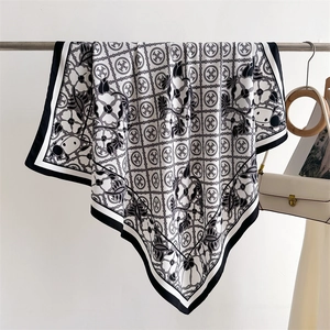 Detail view of monochrome floral silk scarf with geometric star patterns on a display stand