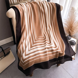 Elegant long silk shawl with geometric stripes draped over a sofa in warm coffee tones