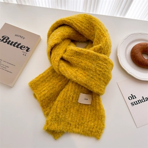 Minimalist yellow wool knit scarf with soft texture and white label on a white table