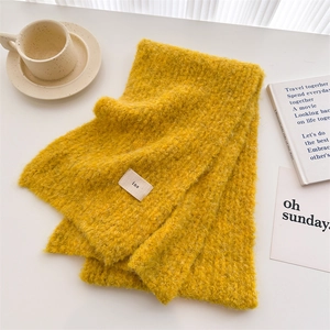 Detail of fluffy yellow knit scarf texture with a woven label on a white table