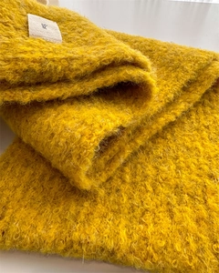 Close-up of bright yellow knit scarf showing fuzzy mohair texture and a small woven label