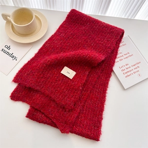 Detail of bright red chunky knit scarf with fabric tag on a cozy lifestyle desk setup
