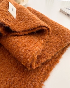Detail of burnt orange thick fuzzy wool scarf featuring a minimalist white woven label
