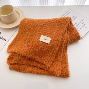 Close-up of bright orange textured wool scarf with minimalist ins woven label detail