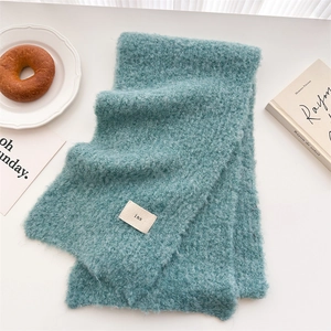 Detailed texture of blue-green mohair knit scarf with minimalist rectangular ins fabric label