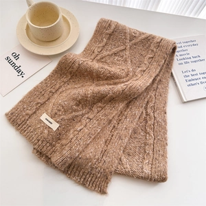Detail shot of chunky cable knit wool scarf texture in camel with a branded woven label