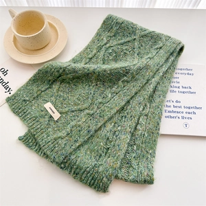 Detailed macro view of green cable knit wool scarf texture with brand label and fiber flecks