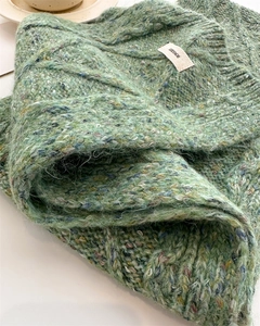 Close-up of green chunky knit wool scarf with speckled texture and brand woven label