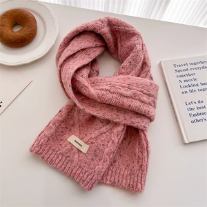 Pink chunky knit wool scarf with cable texture and brand label on a white table