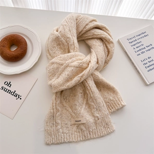 Close-up of beige cable knit wool scarf texture with branding label on a stylish table
