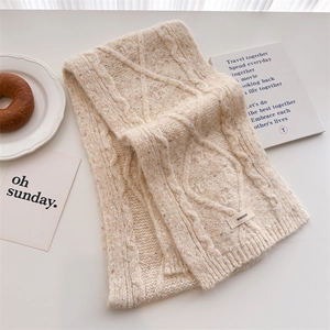 Detailed macro shot of cream knit wool scarf featuring cable and diamond pattern textures
